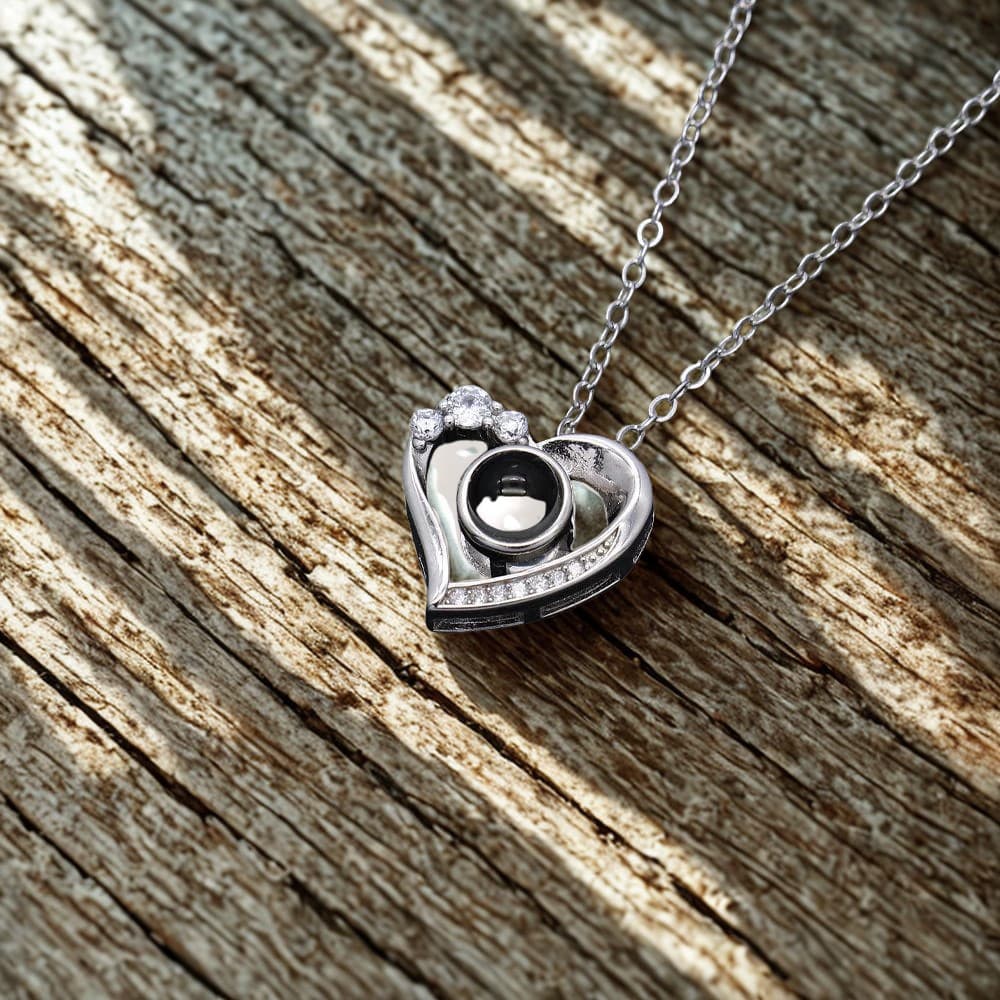 Heart-shaped silver pendant with a camera design on a wooden surface