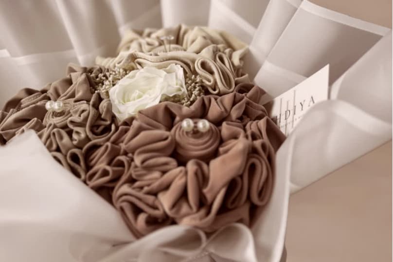 Bouquet of brown fabric Hijabs or khimaars with a white flower in the center, wrapped in white paper.